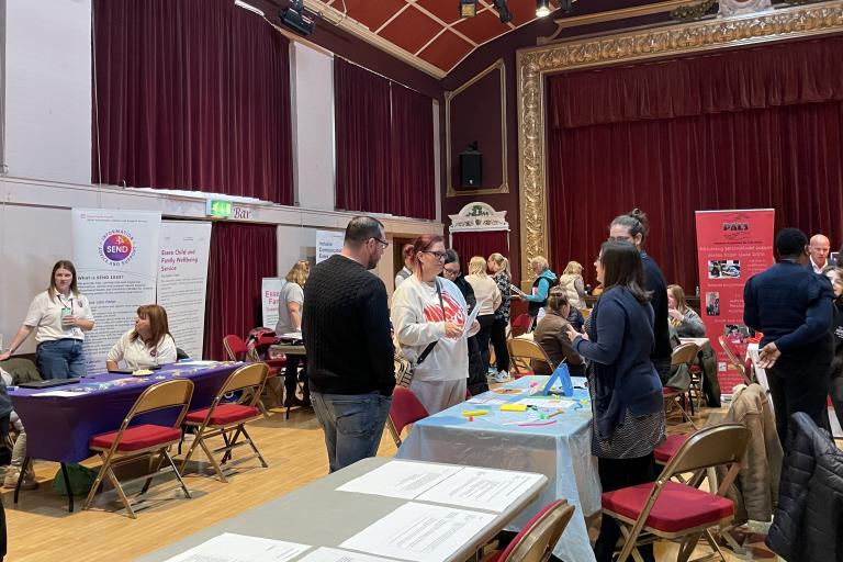 A room full of people at a roadshow talking at various stalls about SEND support