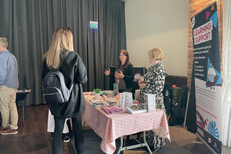 Two people behind a table speaking to an attendee about learning support 