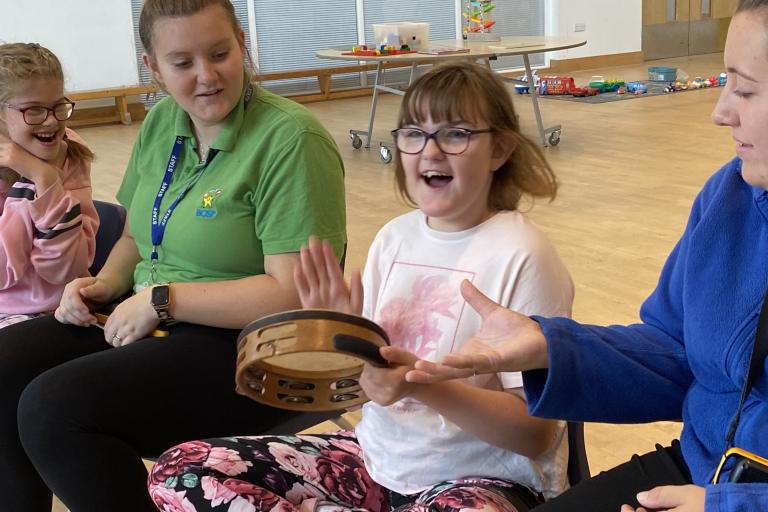 Children playing tambourines and other instruments with instructors helping them