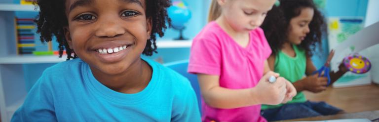 Photograph of three children smiling, drawing and playing